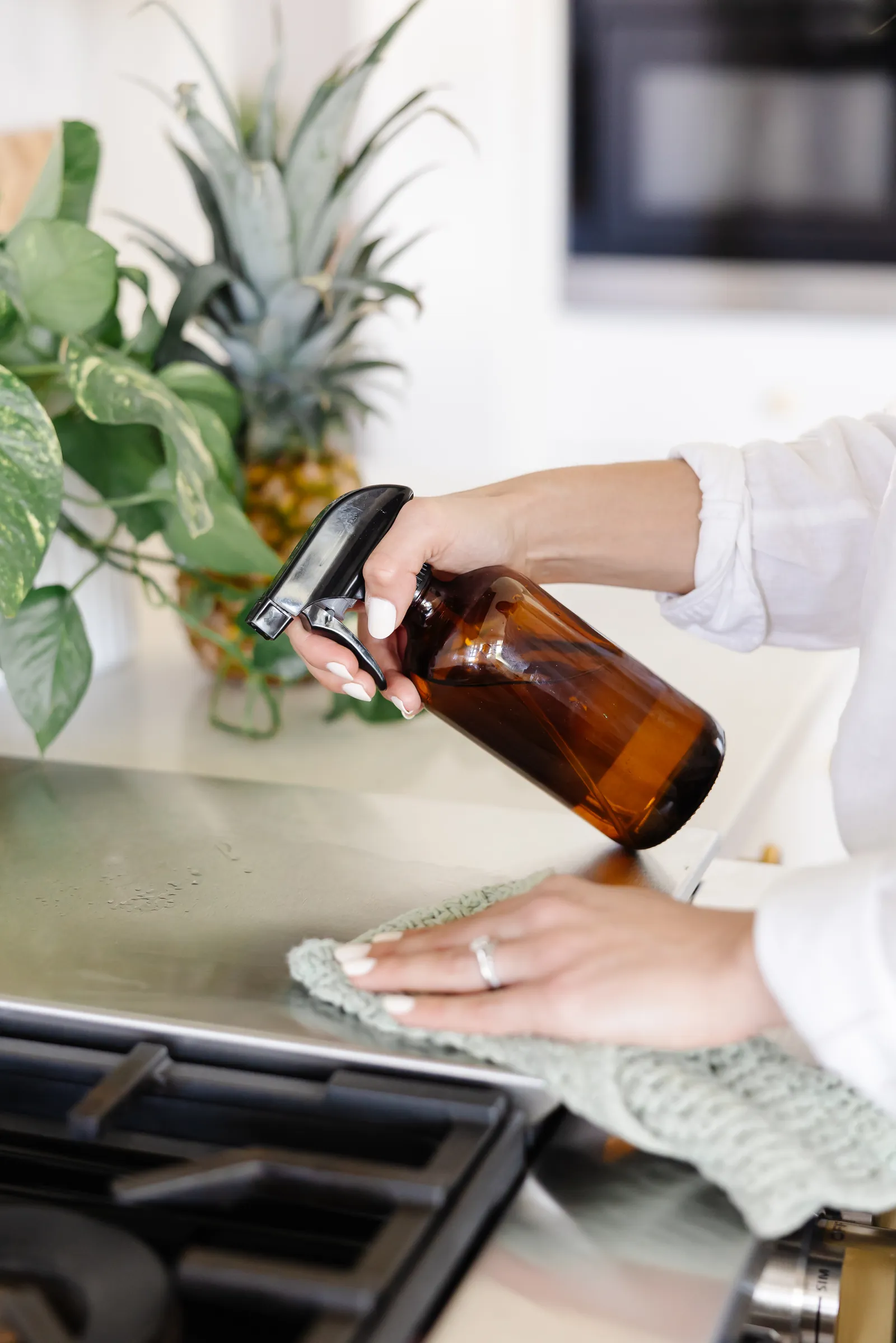 Alicia wiping the stovetop with an amber-glass spray bottle and a reusable cloth