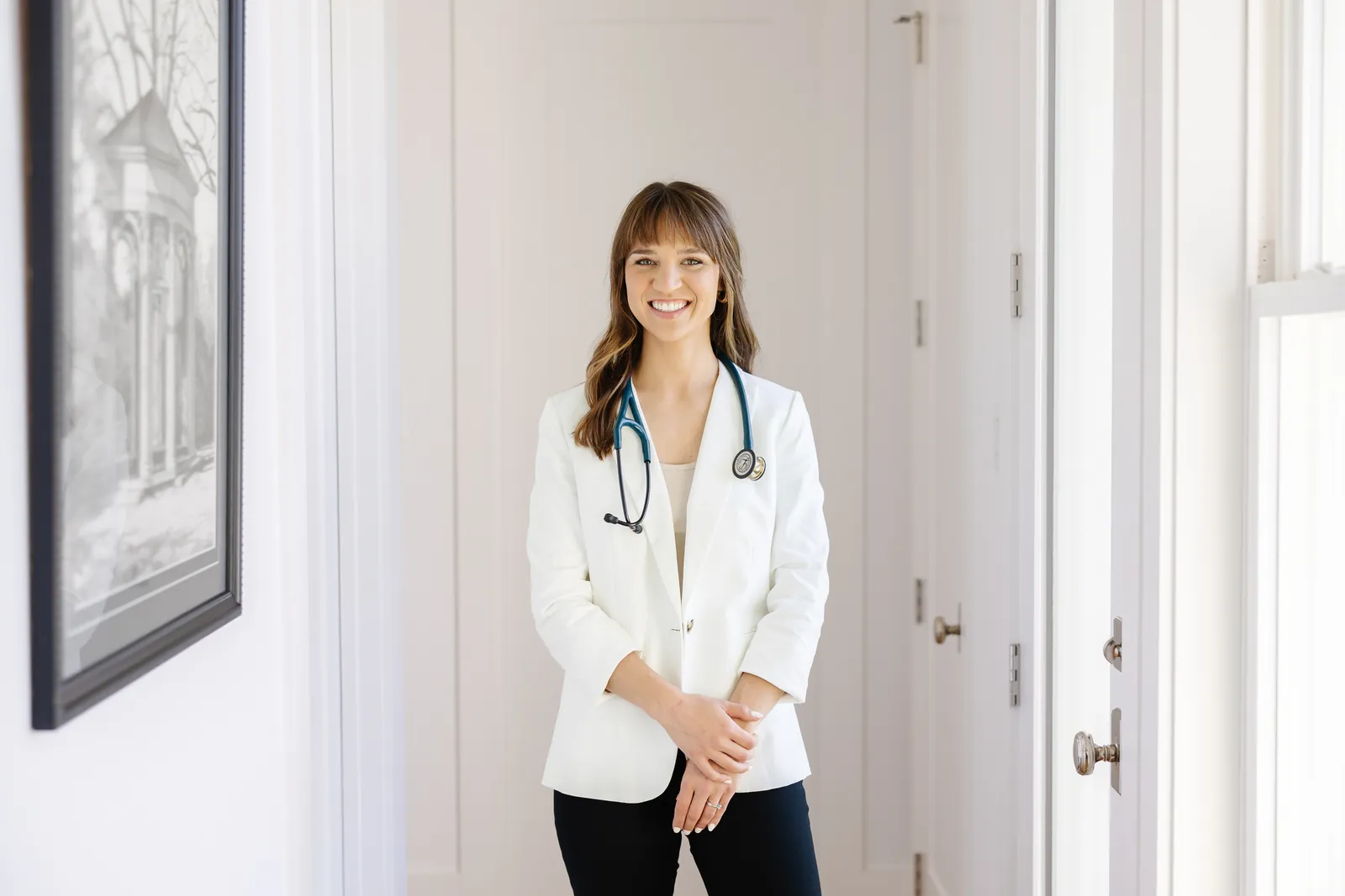 Alicia Harrison in a white blazer with a stethoscope around her neck, smiling in bright natural light