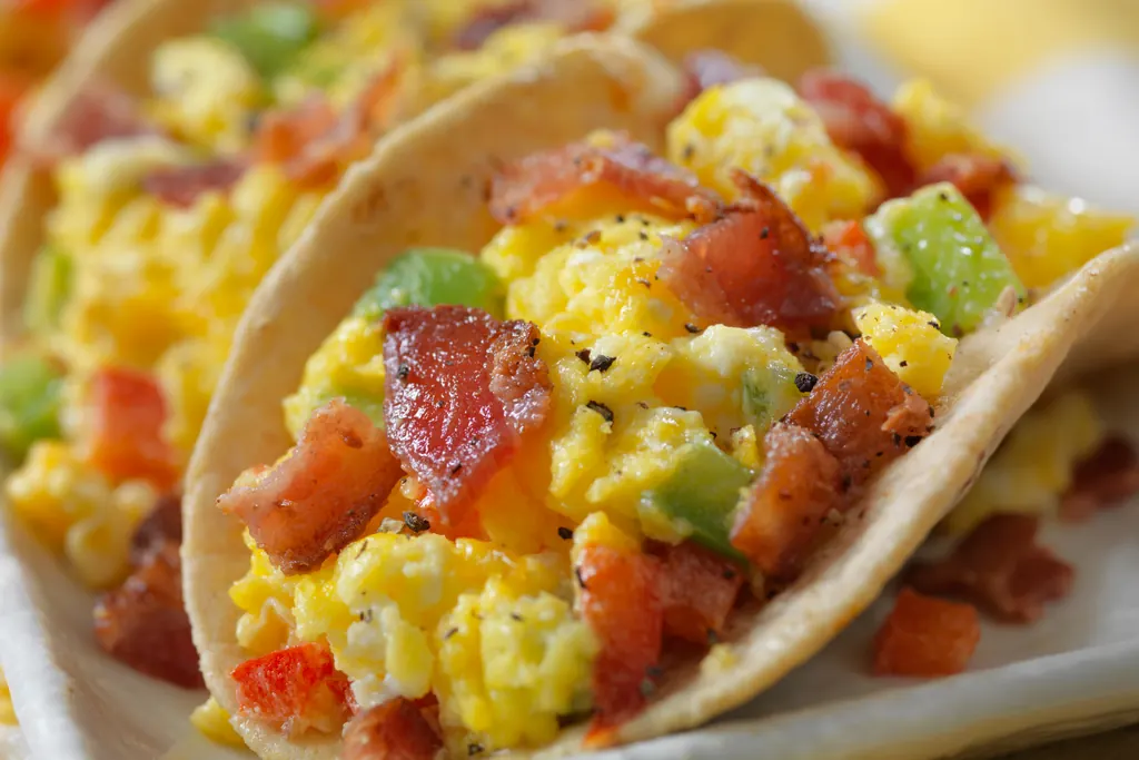 Breakfast tacos filled with scrambled eggs, bacon, and diced peppers in warm light
